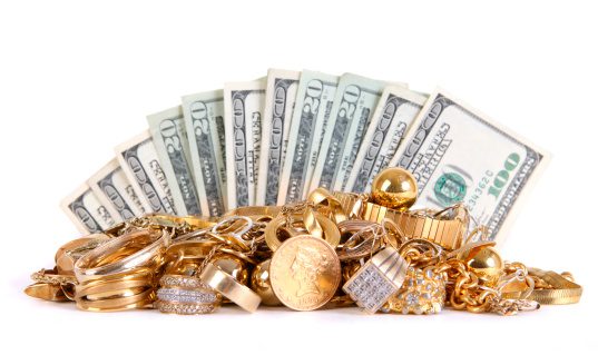 Pile of gold jewelry and luxury items in front of fanned out U.S. hundred-dollar bills