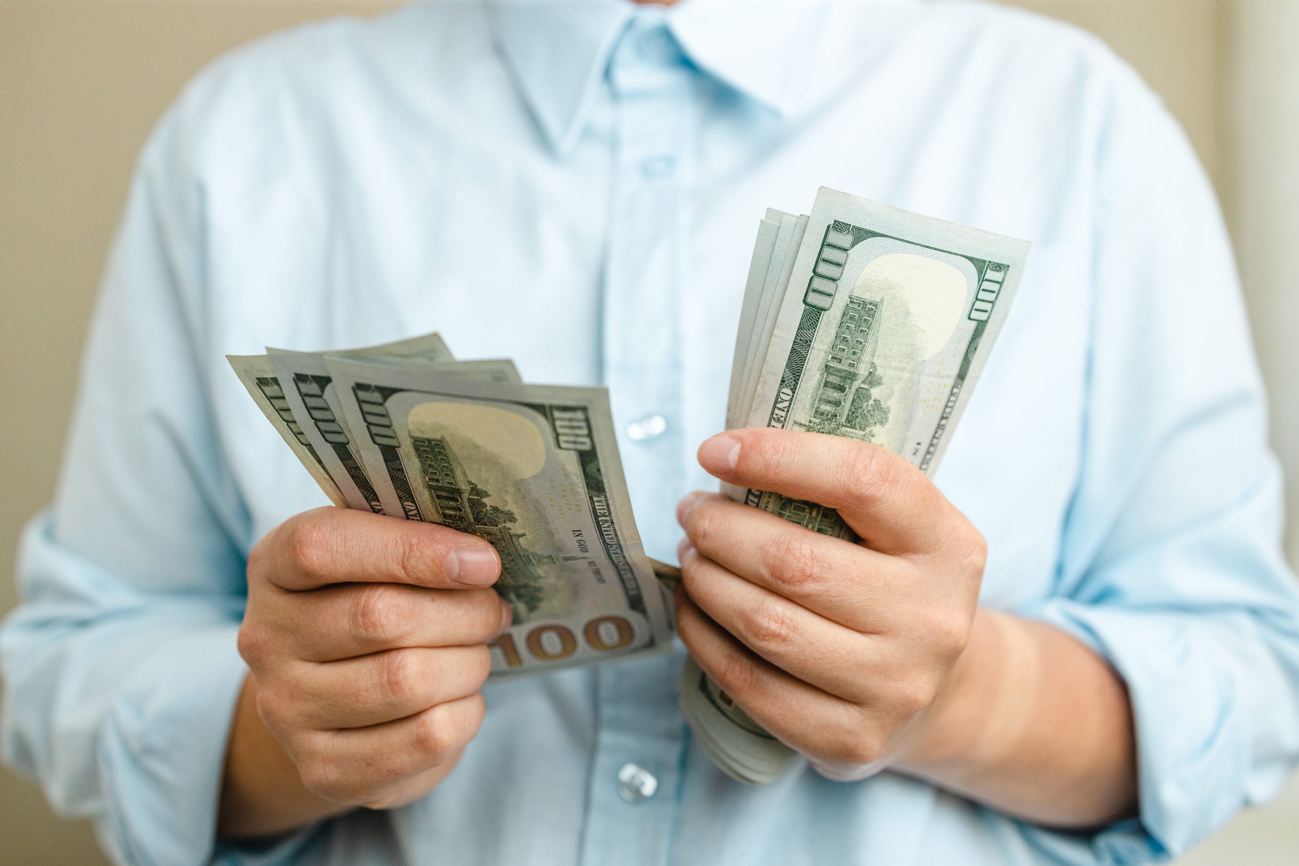 Close-up of a person in a light blue shirt holding multiple stacks of $100 U.S. dollar bills.
