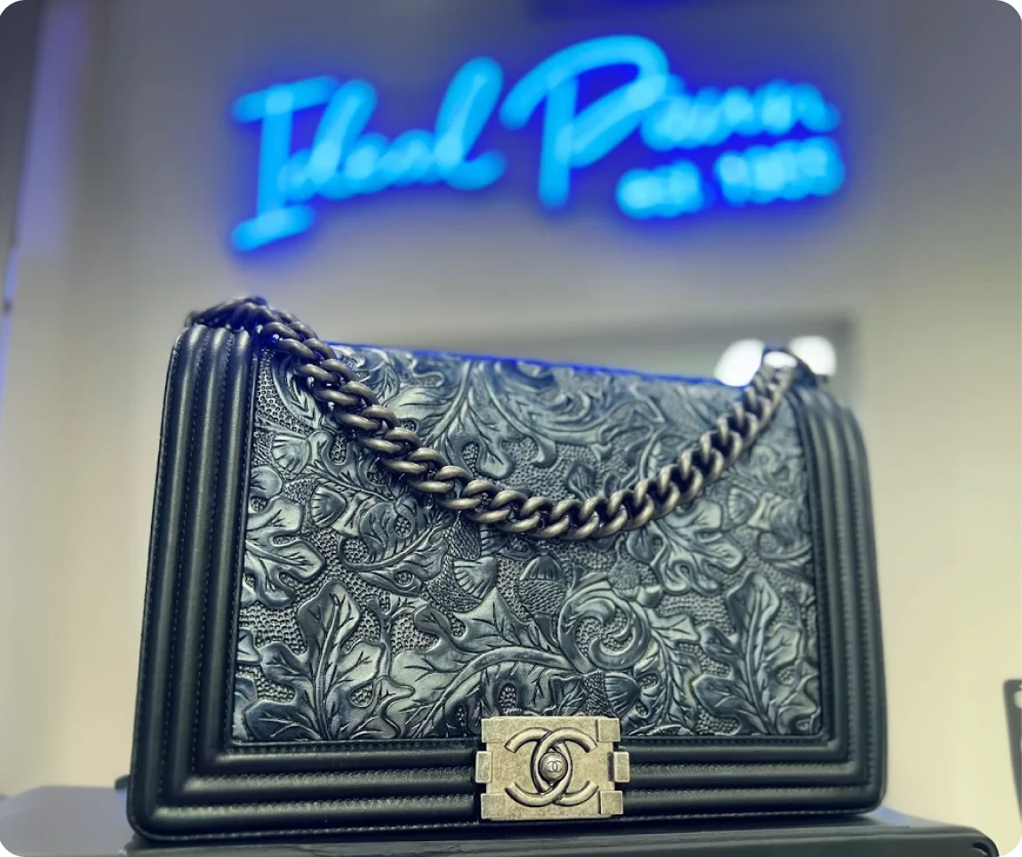 A luxurious black leather handbag with a gold clasp, sitting in front of a sign reading 'Brockton MA' in a modern, neon-lit